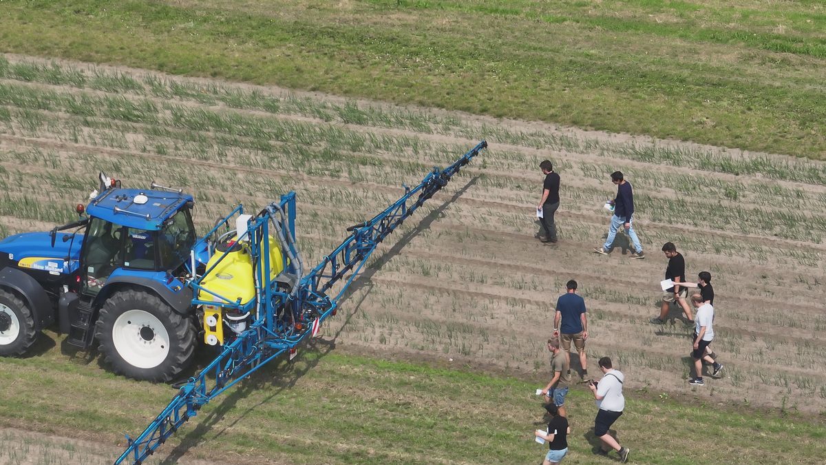 Een groep landbouwers bij een veldspuit op een proefveld.