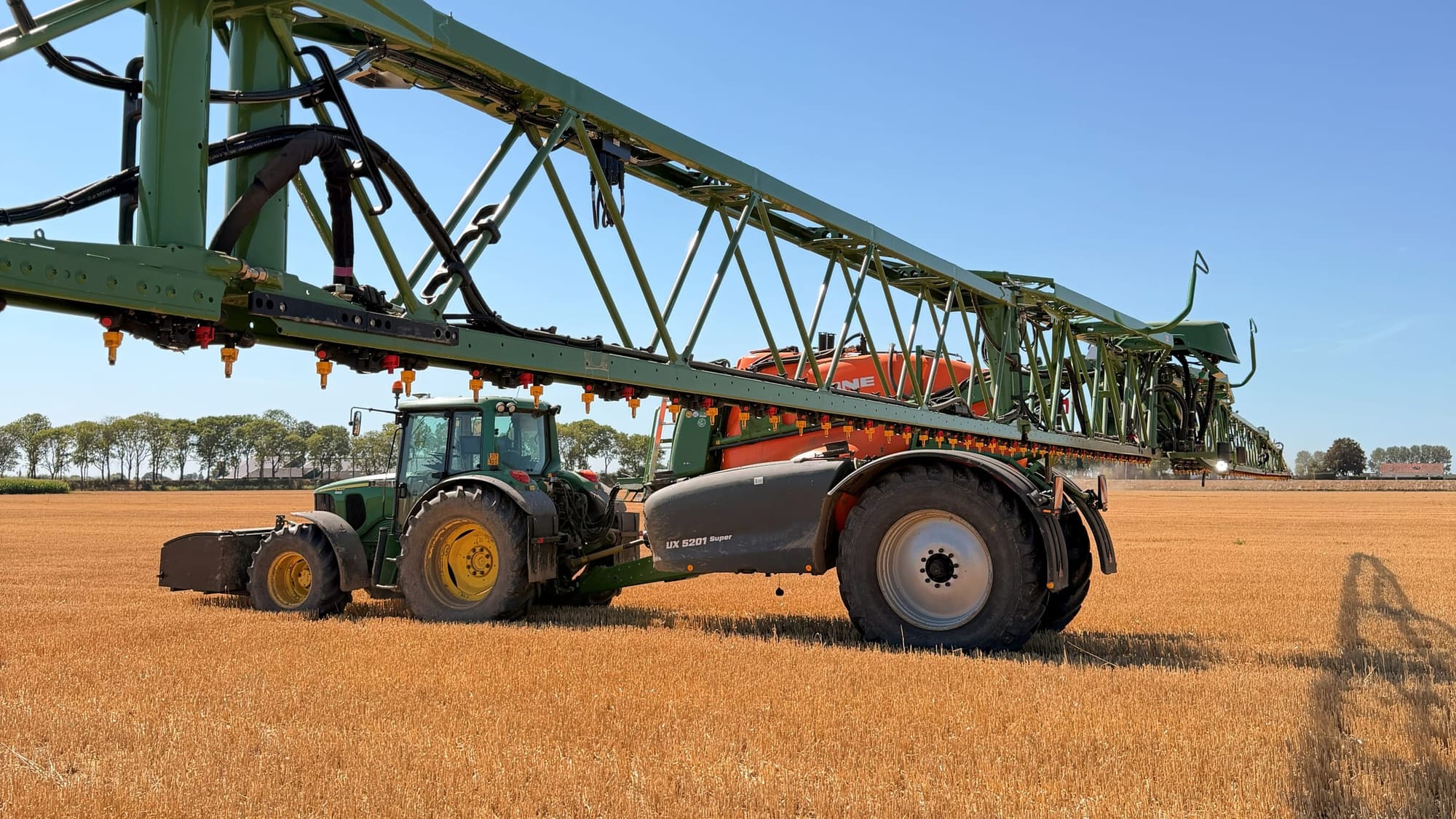 Un tracteur avec un pulvérisateur déployé sur une parcelle de chaumes.