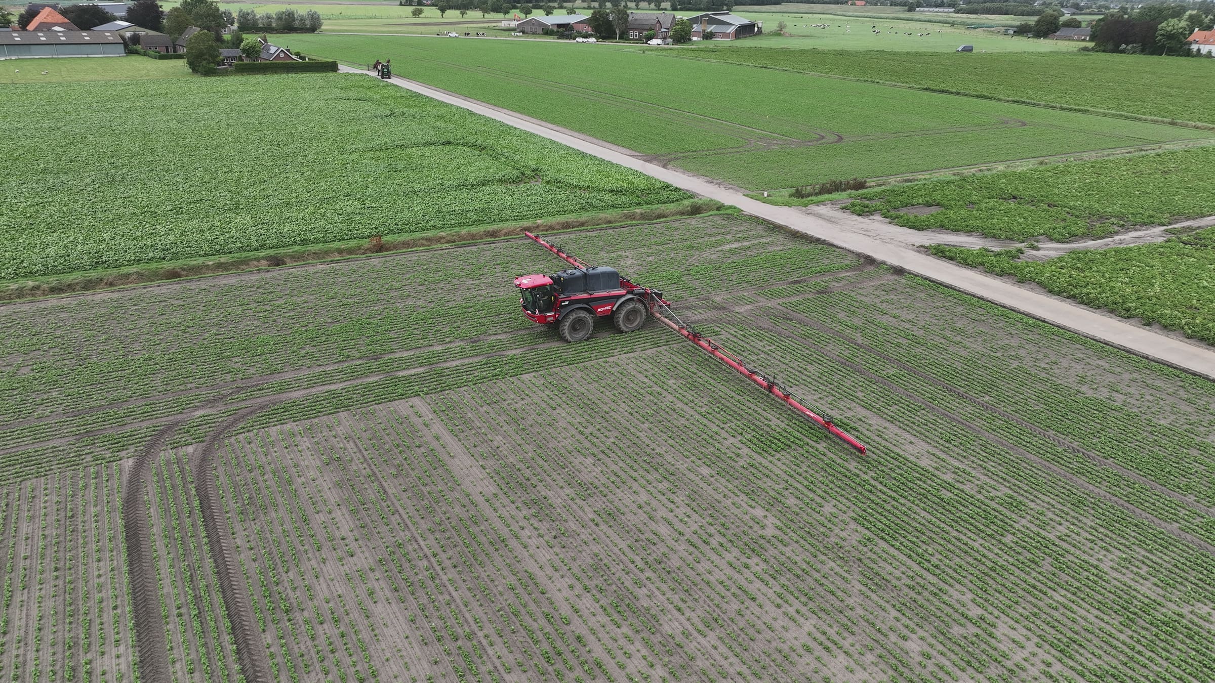 Red field sprayer driving through a field, seen from the drone